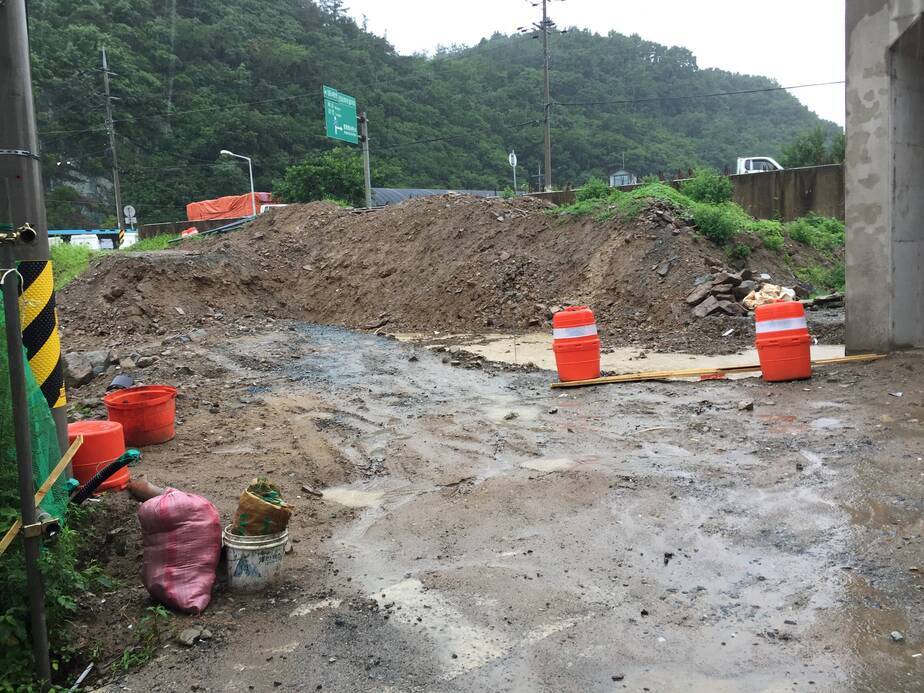 진흙이 가득한 길이 중앙에 보이고 뒤로는 흙이 높게 쌓여있으며 뒤로는 산과 이정표가 보이는 모습