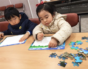 초등학생 2명의 어린이가 의자에 앉아 퍼즐을 맞추기 위해 퍼즐조각을 만지는 모습